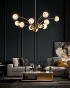 A lit Clérachic chandelier with textured globes in a charcoal room, with grey sofas, a brass-edged coffee table and a floral artwork.