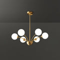 A Clérachic chandelier with six white globes on a brass rod, shown against a dark grey studio backdrop.