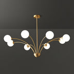 A larger Clérachic brass chandelier with white globes on long curving arms, shown against a dark grey studio backdrop.