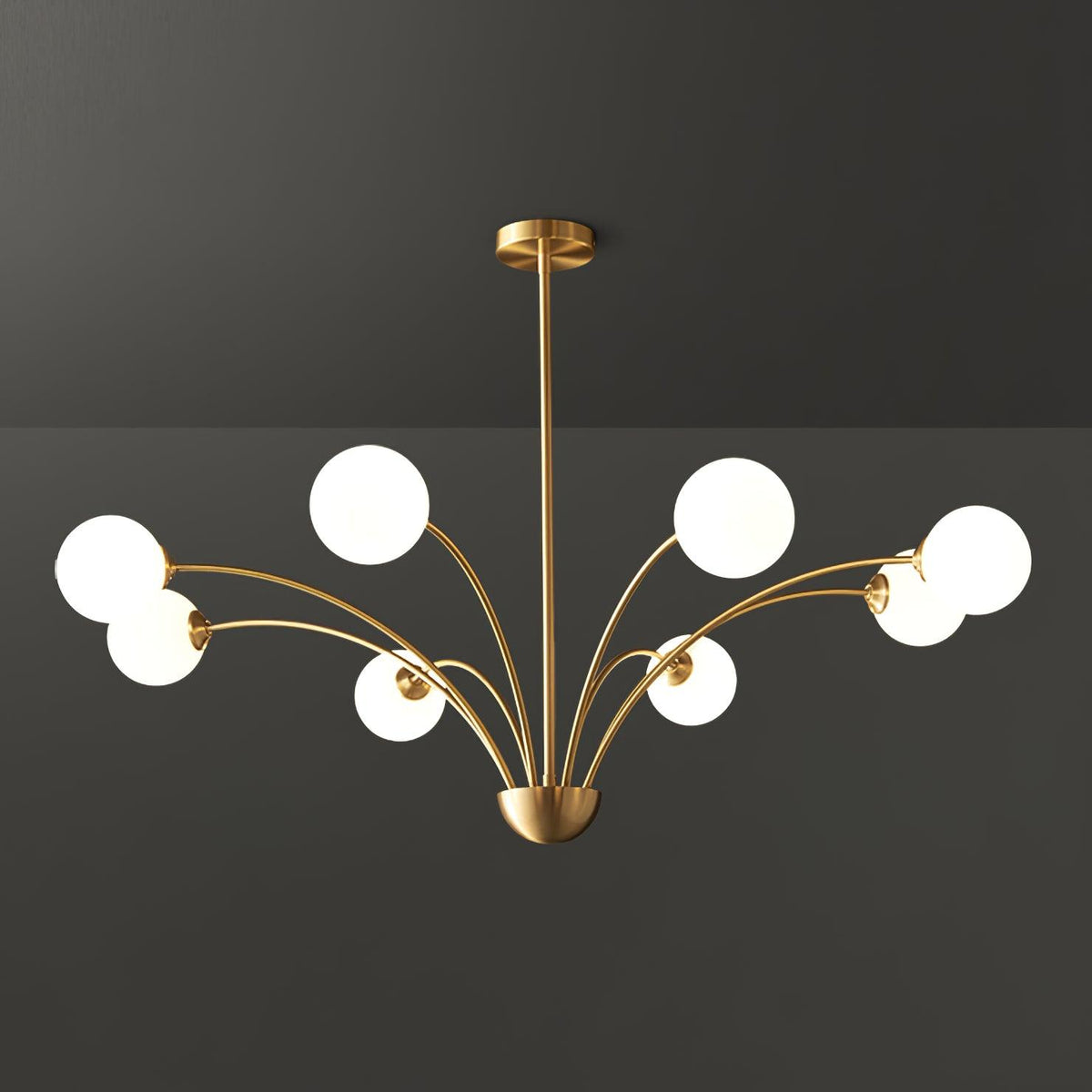A larger Clérachic brass chandelier with white globes on long curving arms, shown against a dark grey studio backdrop.
