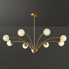 A Clérachic brass chandelier with textured globes on long sweeping arms, photographed against a dark grey backdrop.