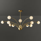 A wide Clérachic brass chandelier with warm, textured globes on layered arms, photographed against a dark grey backdrop.