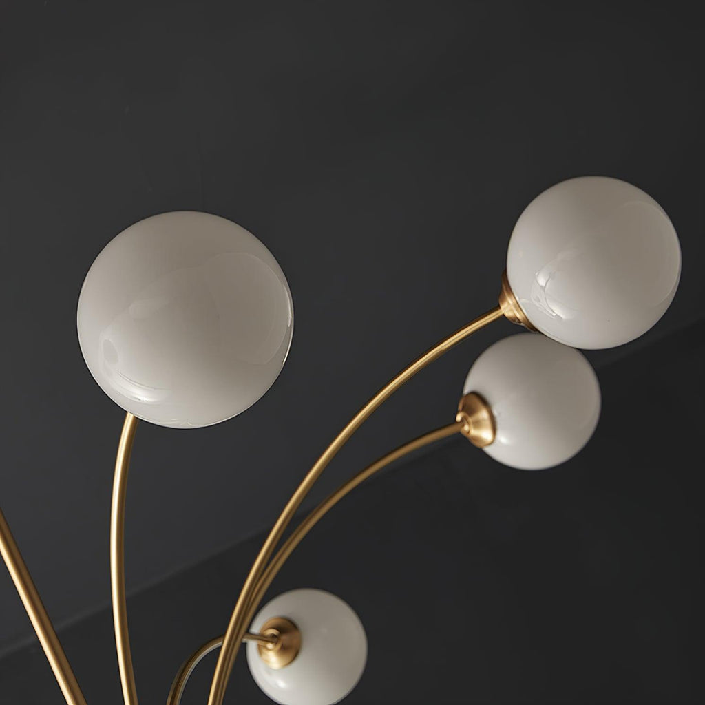 Close view of the white glass globes and slender brass arms on this Clérachic chandelier, seen from below against a dark ceiling.