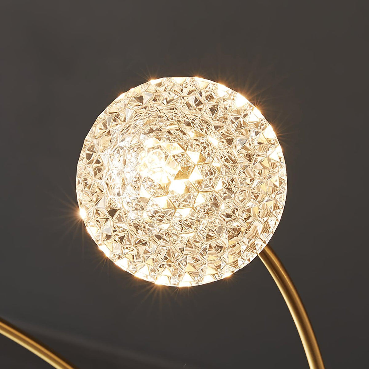 Close view of one lit, faceted globe on this Clérachic chandelier, glittering on a curved brass arm.