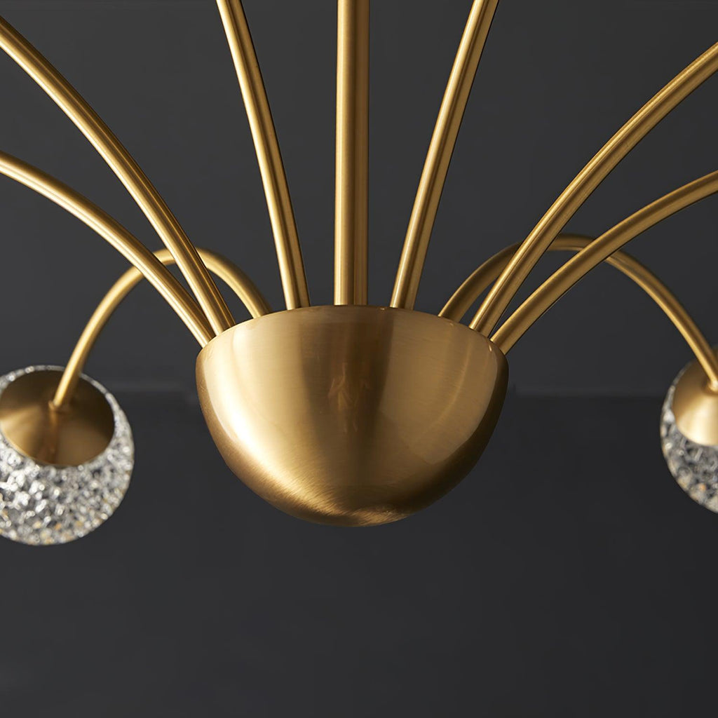 Close view of the brushed brass half-dome hub where the arms of this Clérachic chandelier meet, with glass globes at either edge.