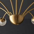 Close view of the brushed brass half-dome hub where the arms of this Clérachic chandelier meet, with glass globes at either edge.