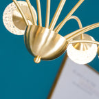 Close view of the brass hub on this Clérachic chandelier, with a lit globe and a framed print blurred against a teal wall.