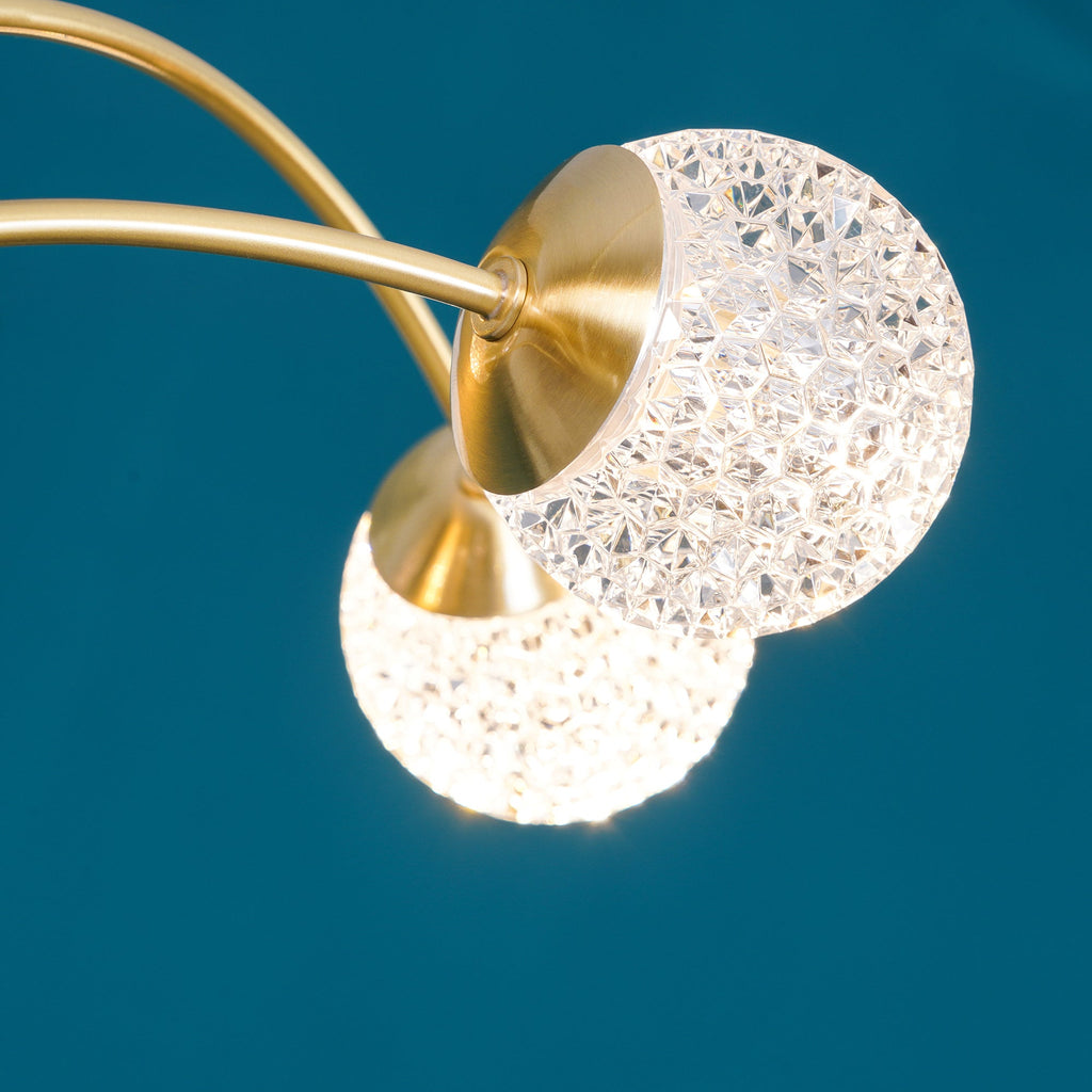 Close view of two textured globes on brass collars, one lit, on this Clérachic chandelier against a teal wall.