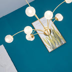 Looking up at the lit globes of this Clérachic chandelier, spreading out over a framed botanical print on a teal wall.
