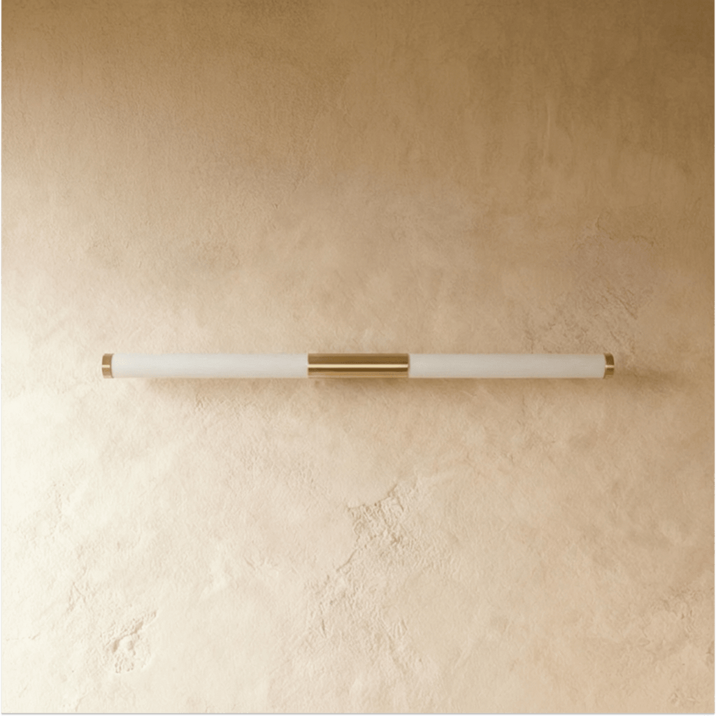 Clérachic slim linear wall light switched off, with a frosted tube and brass centre mount on a warm plaster wall.
