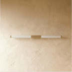 Clérachic slim linear wall light switched off, with a frosted tube and brass centre mount on a warm plaster wall.