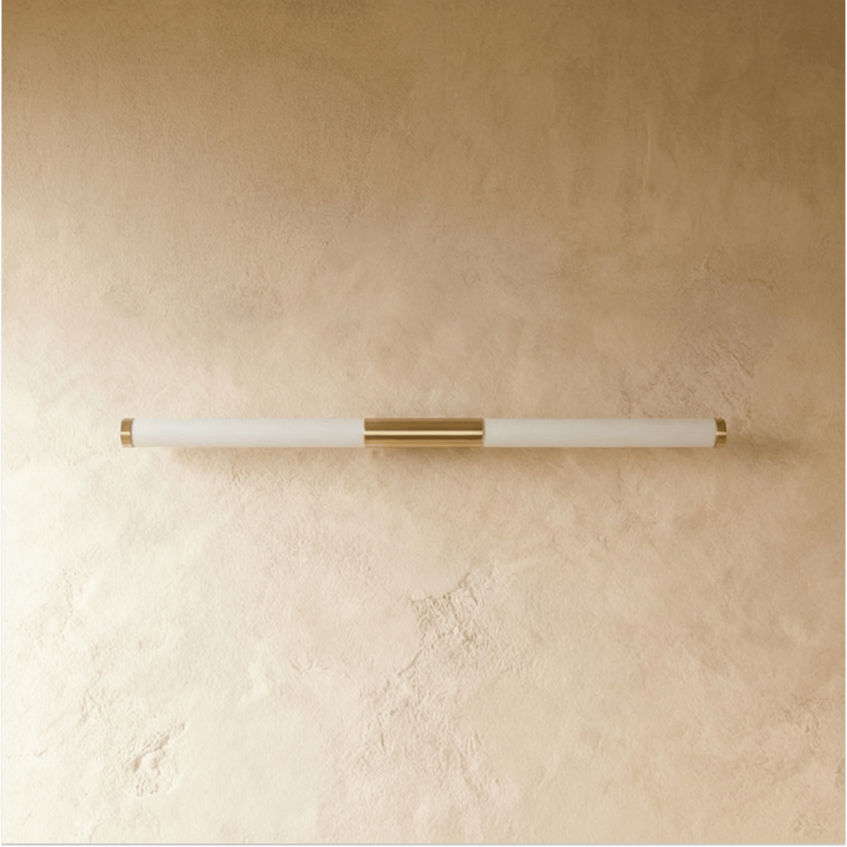 Clérachic slim linear wall light switched off, with a frosted tube and brass centre mount on a warm plaster wall.