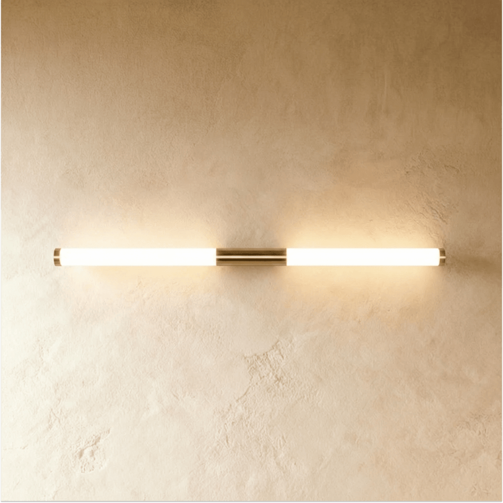 Clérachic linear LED wall light in a longer length, its frosted tube lit warm either side of a brass centre mount.