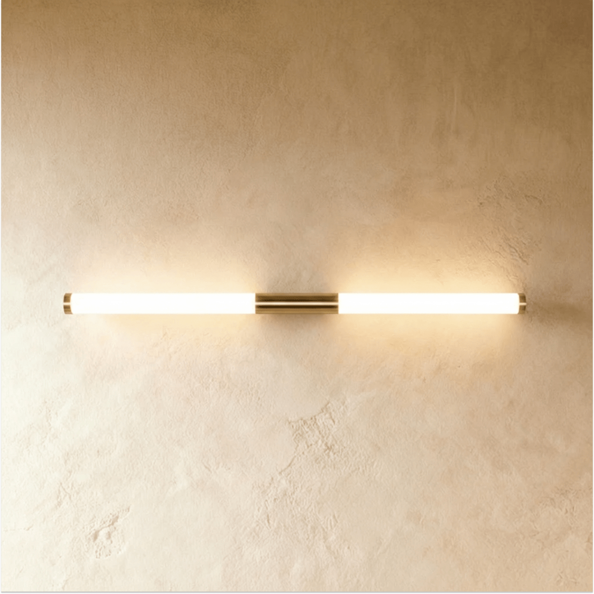 Clérachic linear LED wall light in a longer length, its frosted tube lit warm either side of a brass centre mount.