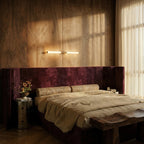 Clérachic slim linear wall light glowing above a plum velvet headboard, on wood-panelled walls beside a sheer curtain.