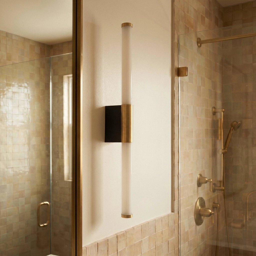 Clérachic slim vertical wall light with a frosted tube, brass collar and black backplate, beside a tiled shower.