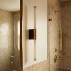 Clérachic slim vertical wall light with a frosted tube, brass collar and black backplate, beside a tiled shower.