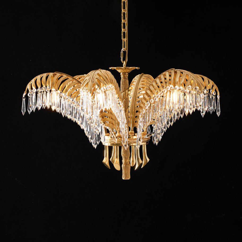 A Clérachic chandelier in lit brass and clear crystal, hung on a gold chain against a black backdrop.