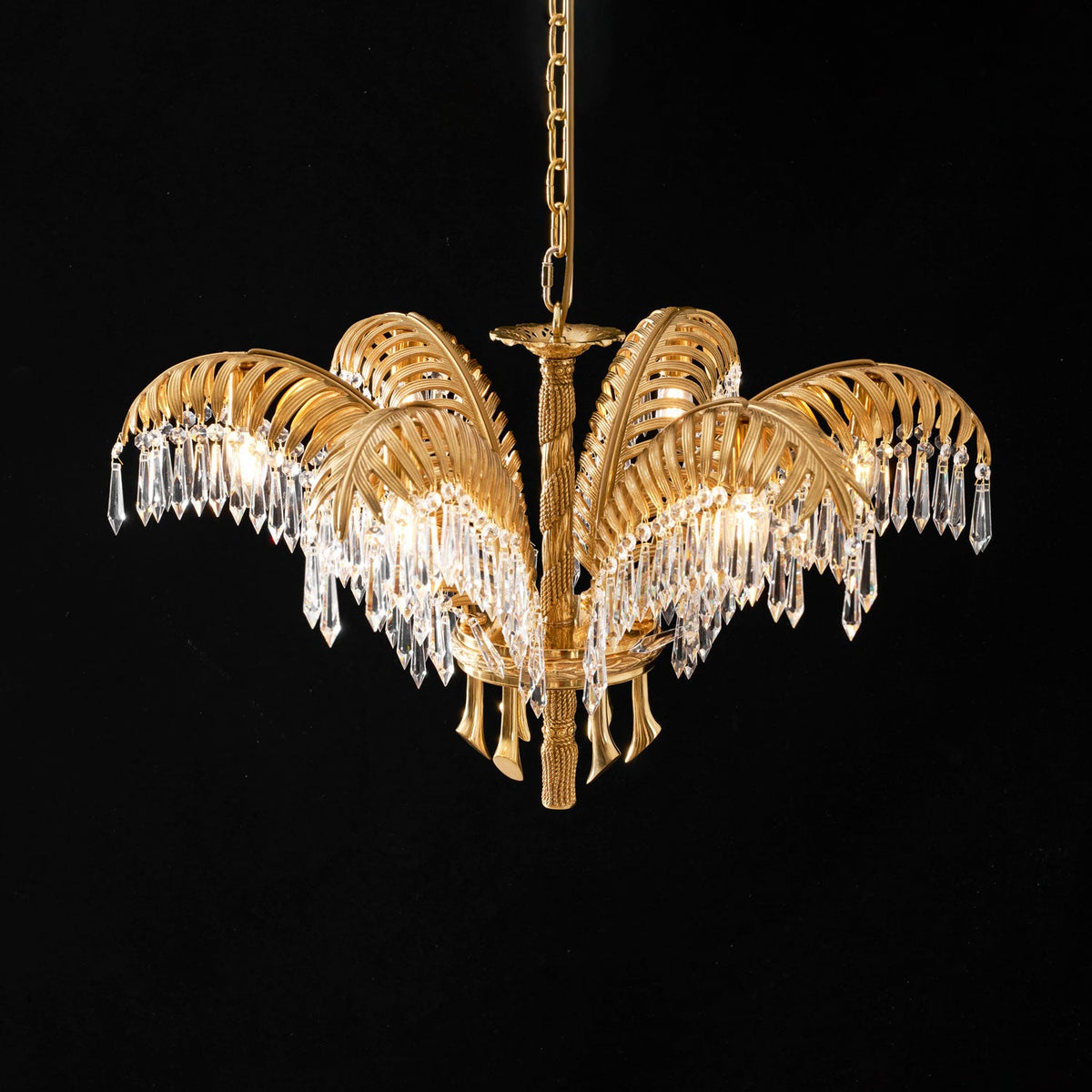 Gold brass leaves with crystal drops on this Clérachic chandelier, lit warmly against a dark background.