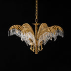 Lit Clérachic chandelier in brass with long crystal drops, hanging on a chain against black.