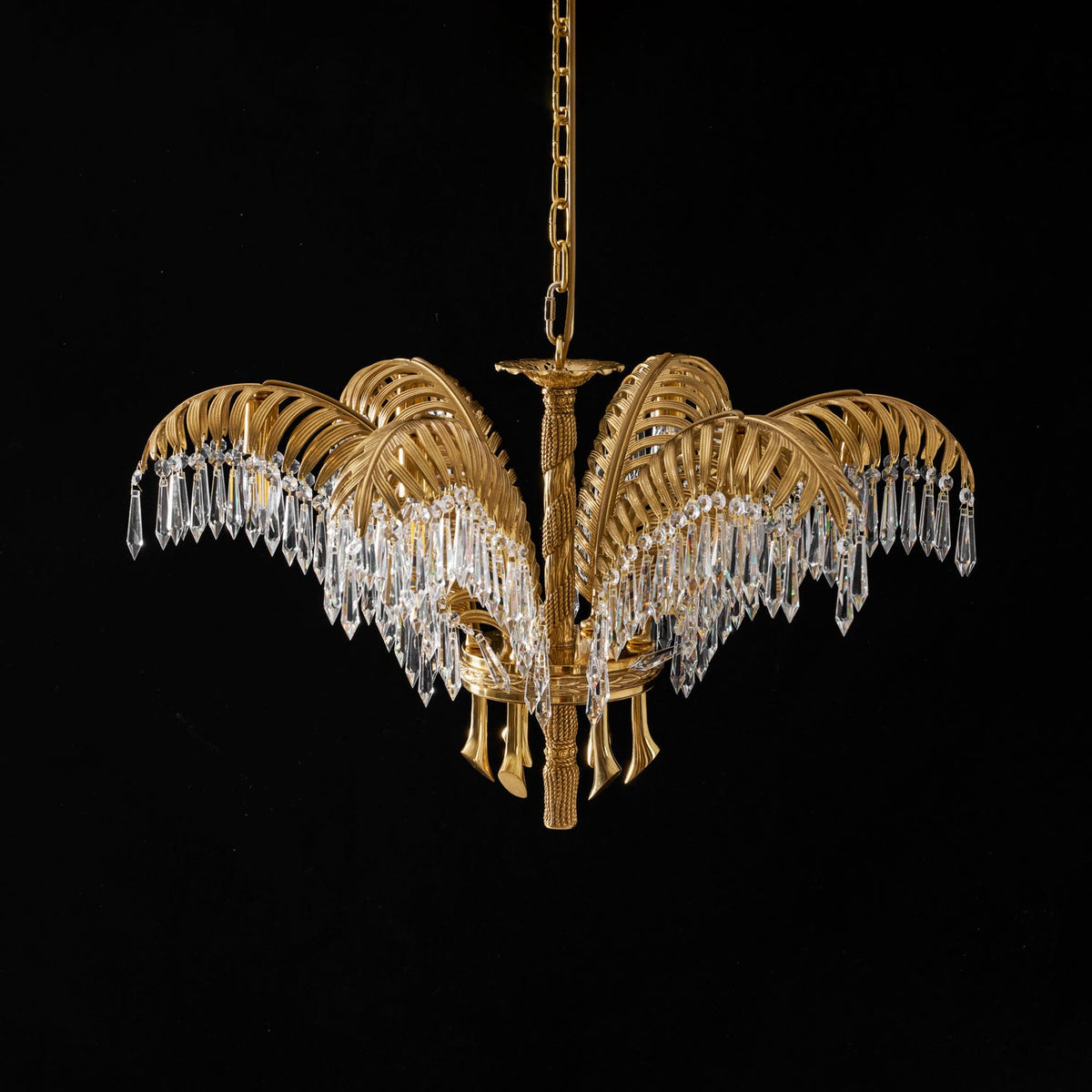 Lit Clérachic chandelier in brass with long crystal drops, hanging on a chain against black.
