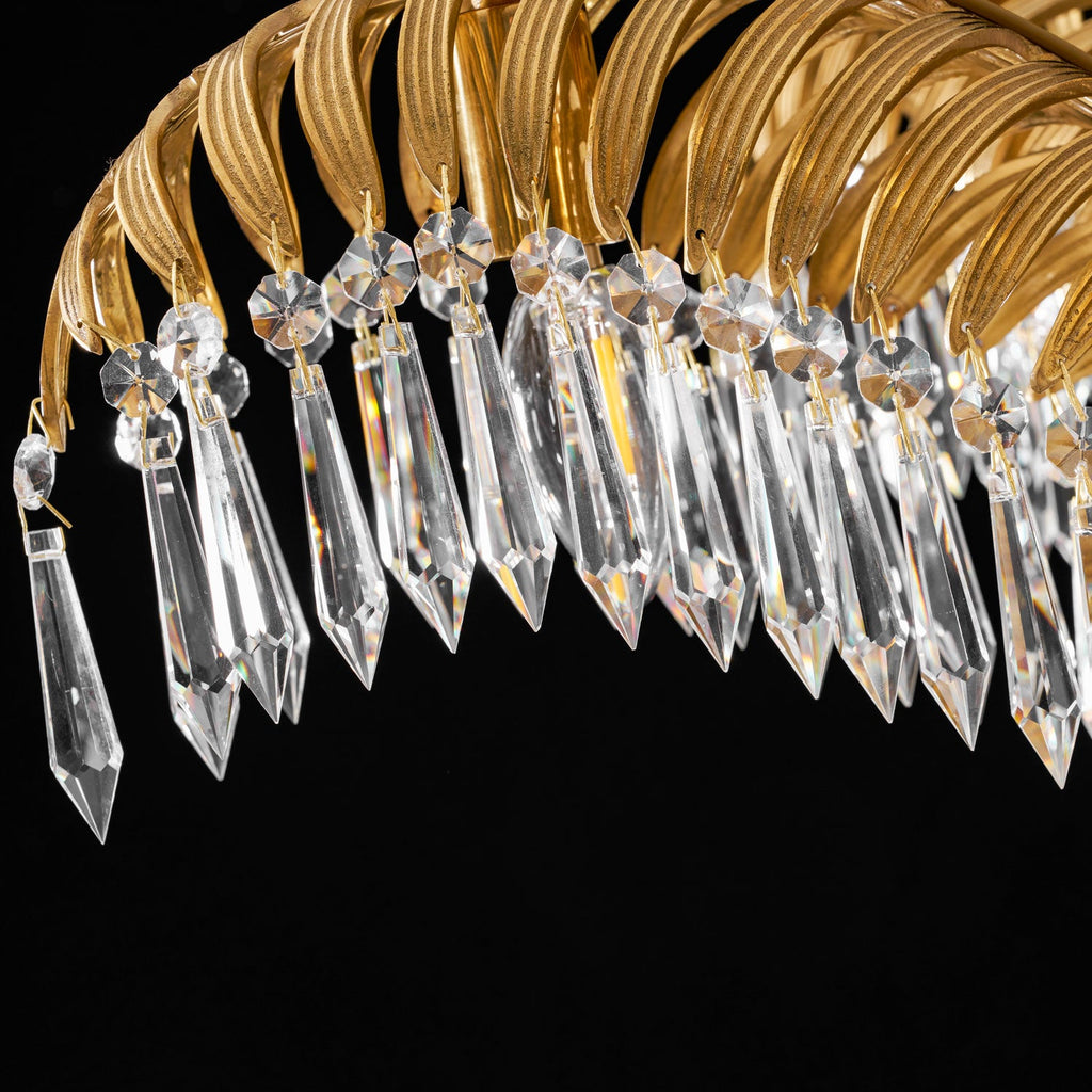 Close view of faceted clear crystal drops hanging from a brass leaf arch on this Clérachic chandelier, against black.
