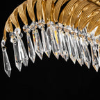 Close view of faceted clear crystal drops hanging from a brass leaf arch on this Clérachic chandelier, against black.