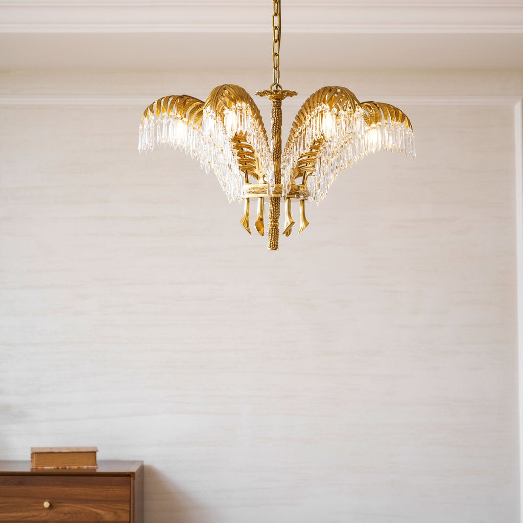 A Clérachic brass chandelier hangs in front of a pale wall above a wooden cabinet with a small wooden box on top.