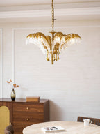 Portrait view of a Clérachic brass chandelier above a wooden sideboard with a vase of dried stems and a book.