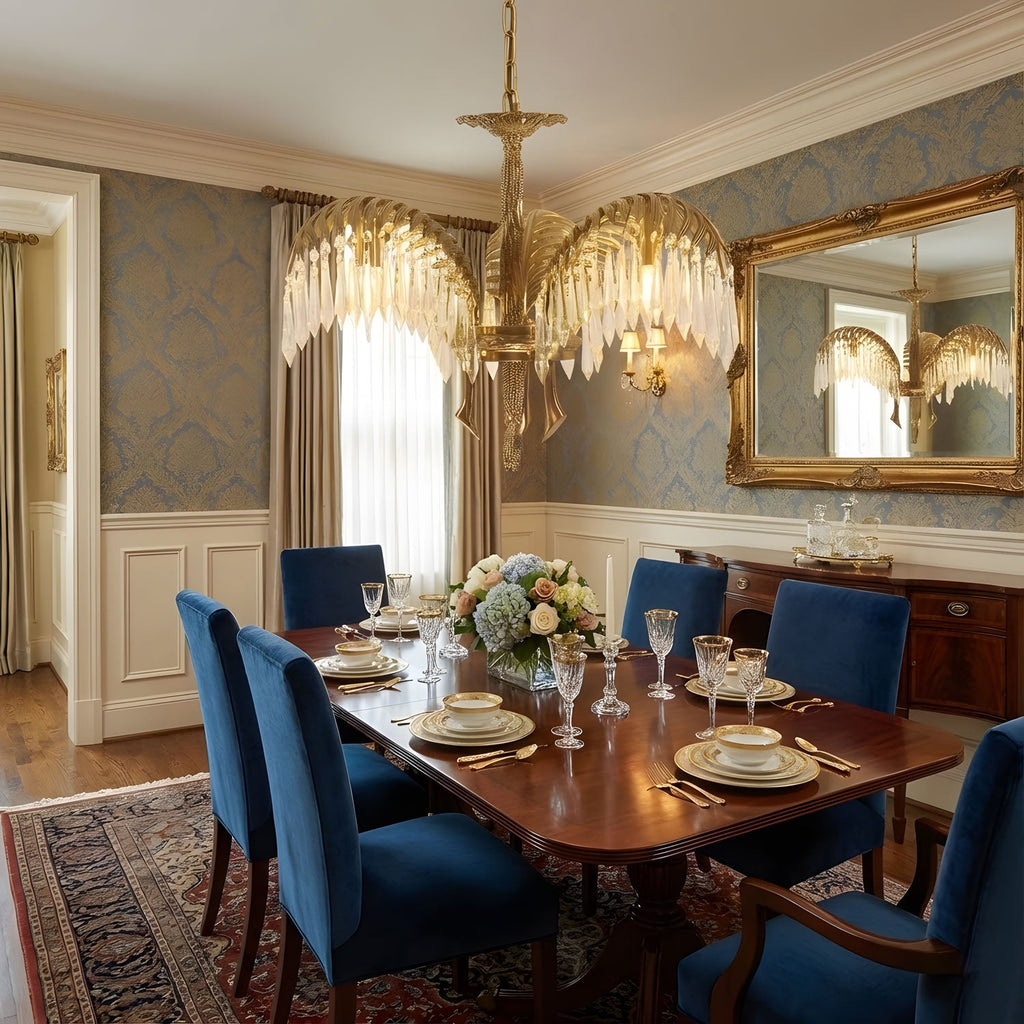 Tiered brass leaves of a Clérachic chandelier hang above a polished wooden dining table set with plates and blue velvet chairs.