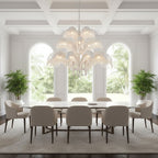A pale, white-toned Clérachic chandelier hangs in a bright room with three arched windows and a long table with cream chairs.