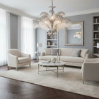A silver-white version of this Clérachic chandelier sits above a round coffee table in a grey living room with cream sofas.