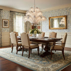 A white-toned Clérachic palm chandelier hangs over a dining table in a room with floral wallpaper and a gilt mirror.