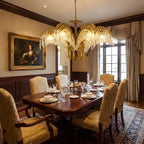 A three-leaf Clérachic brass chandelier hangs in a wood-panelled dining room, a portrait on the wall and a set table below.