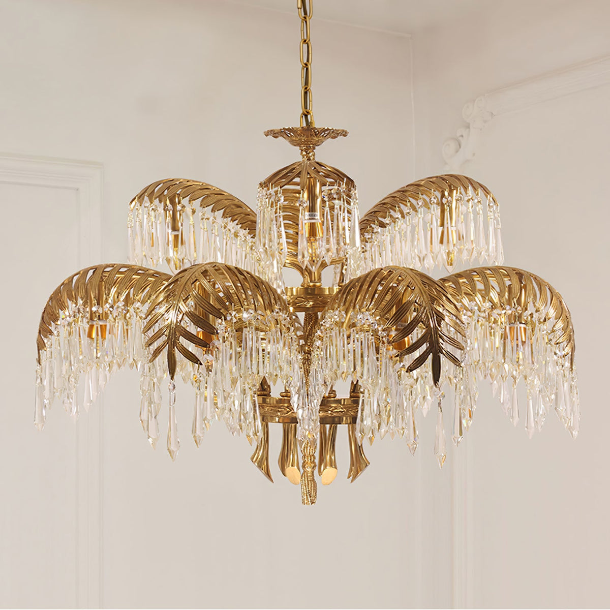Larger tiered Clérachic chandelier in gold brass, with leaf-shaped tiers and long crystal drops against a pale panelled wall.