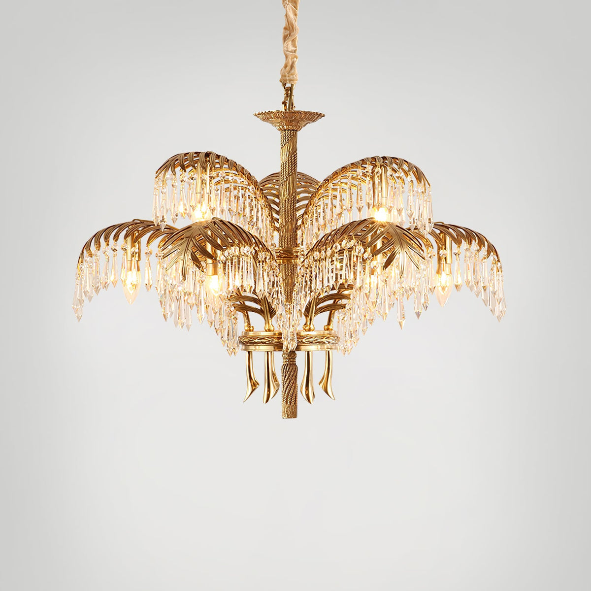 Gold brass Clérachic chandelier with a chain suspension, photographed on a light grey backdrop with its crystal fringes lit.