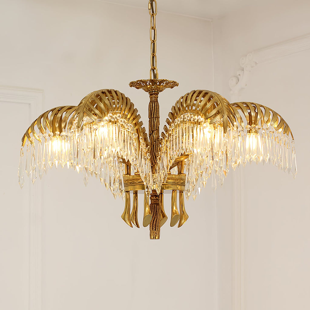 A Clérachic gold brass chandelier on a chain hangs against a pale wall with plaster moulding, its crystal fringes glowing.