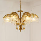 A Clérachic gold brass chandelier on a chain hangs against a pale wall with plaster moulding, its crystal fringes glowing.