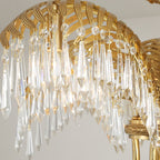 Close view of the ribbed brass leaf arch and the long clear crystal drops hanging from it on this Clérachic chandelier.