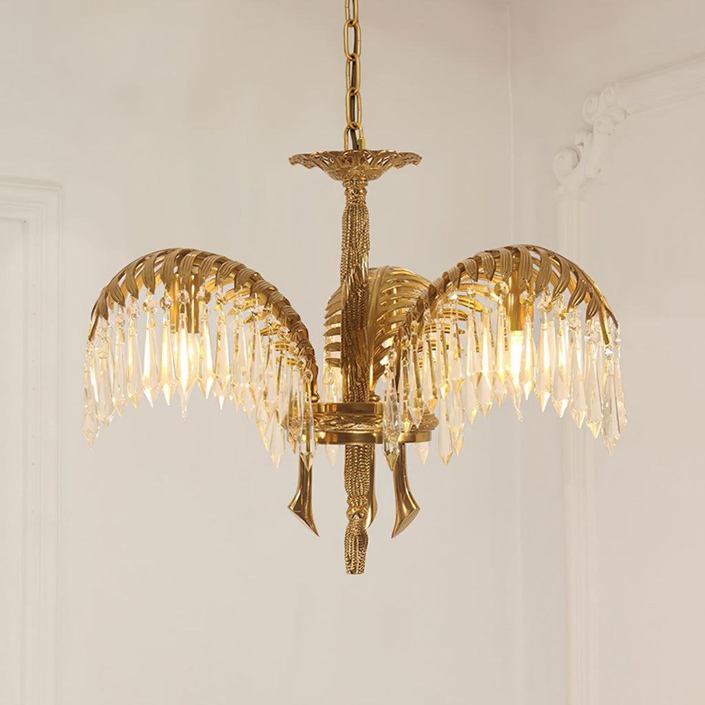 A three-leaf Clérachic chandelier in aged brass on a gold chain, with crystal drops and curved brass tails below.