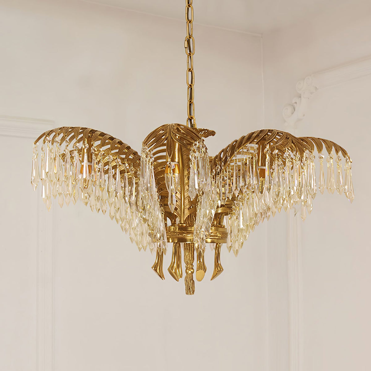 A compact Clérachic brass chandelier with crystal-fringed leaves hangs on a chain against a pale panelled wall.