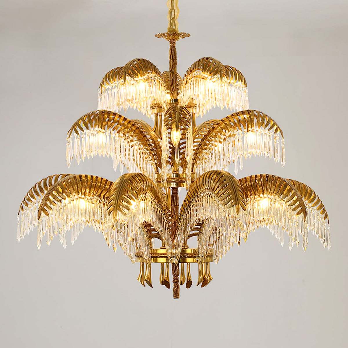 Gold brass Clérachic chandelier in three tiers with crystal drops, on a soft grey backdrop.