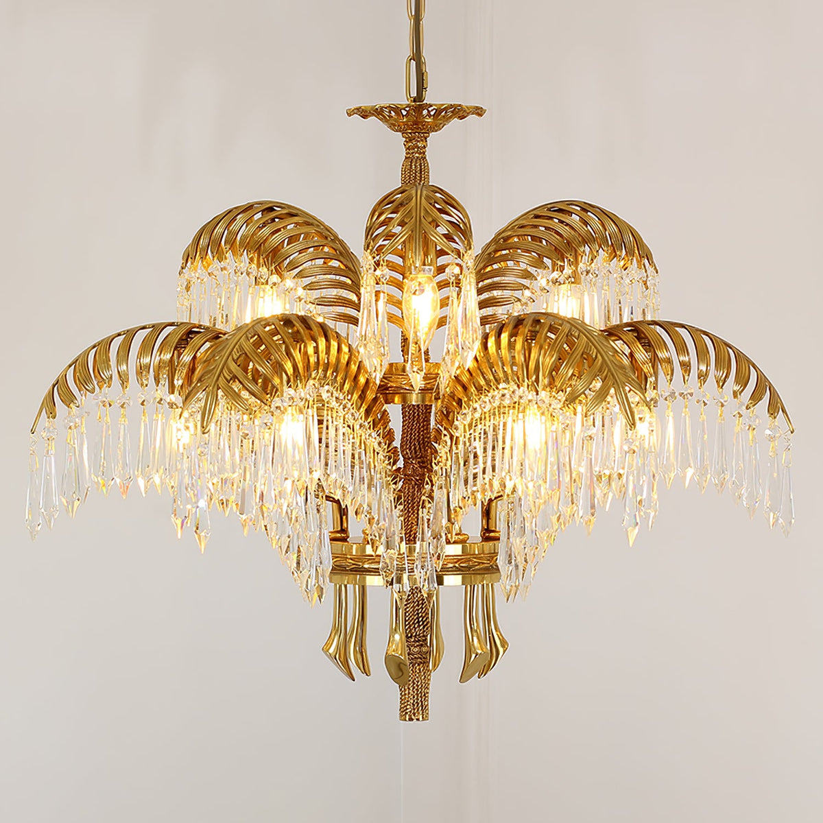 Tiered gold brass Clérachic chandelier with crystal-fringed leaves, photographed on a warm beige backdrop.