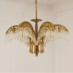 A Clérachic chandelier in gold brass hangs from a chain against a cream wall with plaster moulding.