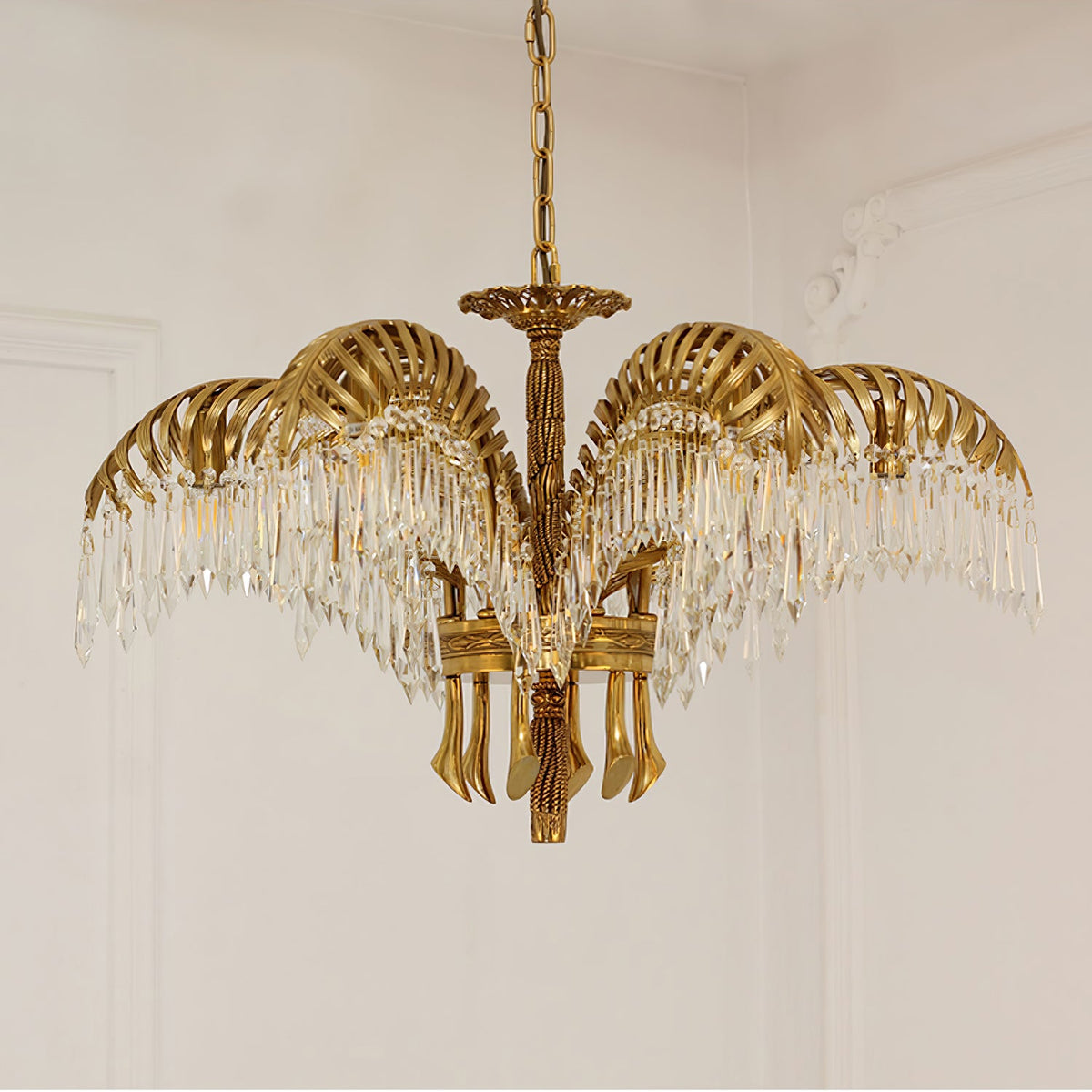 A Clérachic chandelier in gold brass hangs from a chain against a cream wall with plaster moulding.
