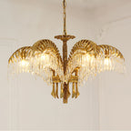Lit from within, this Clérachic gold brass chandelier shows its crystal-fringed leaves in front of a pale moulded wall.