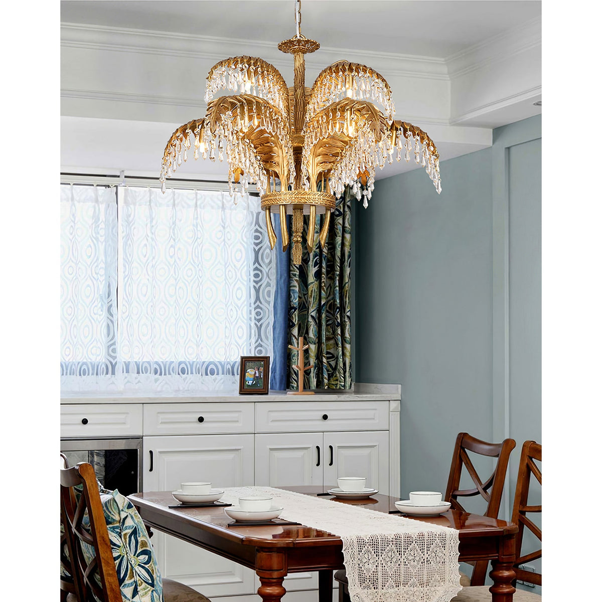 Clérachic brass chandelier over a dining table with a lace runner, in a room with white cabinets and blue-grey walls.