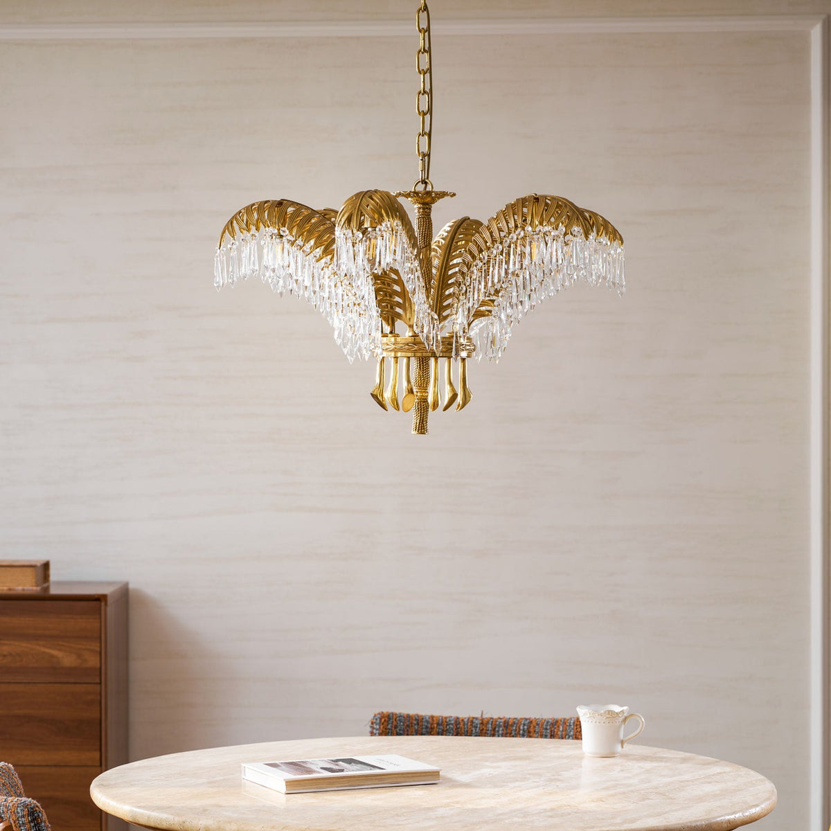 Lower, closer angle of a Clérachic brass chandelier above a round table with a book and a white cup.