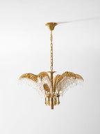 A Clérachic brass chandelier with a carved ceiling plate hangs on a gold chain against a pale grey backdrop.