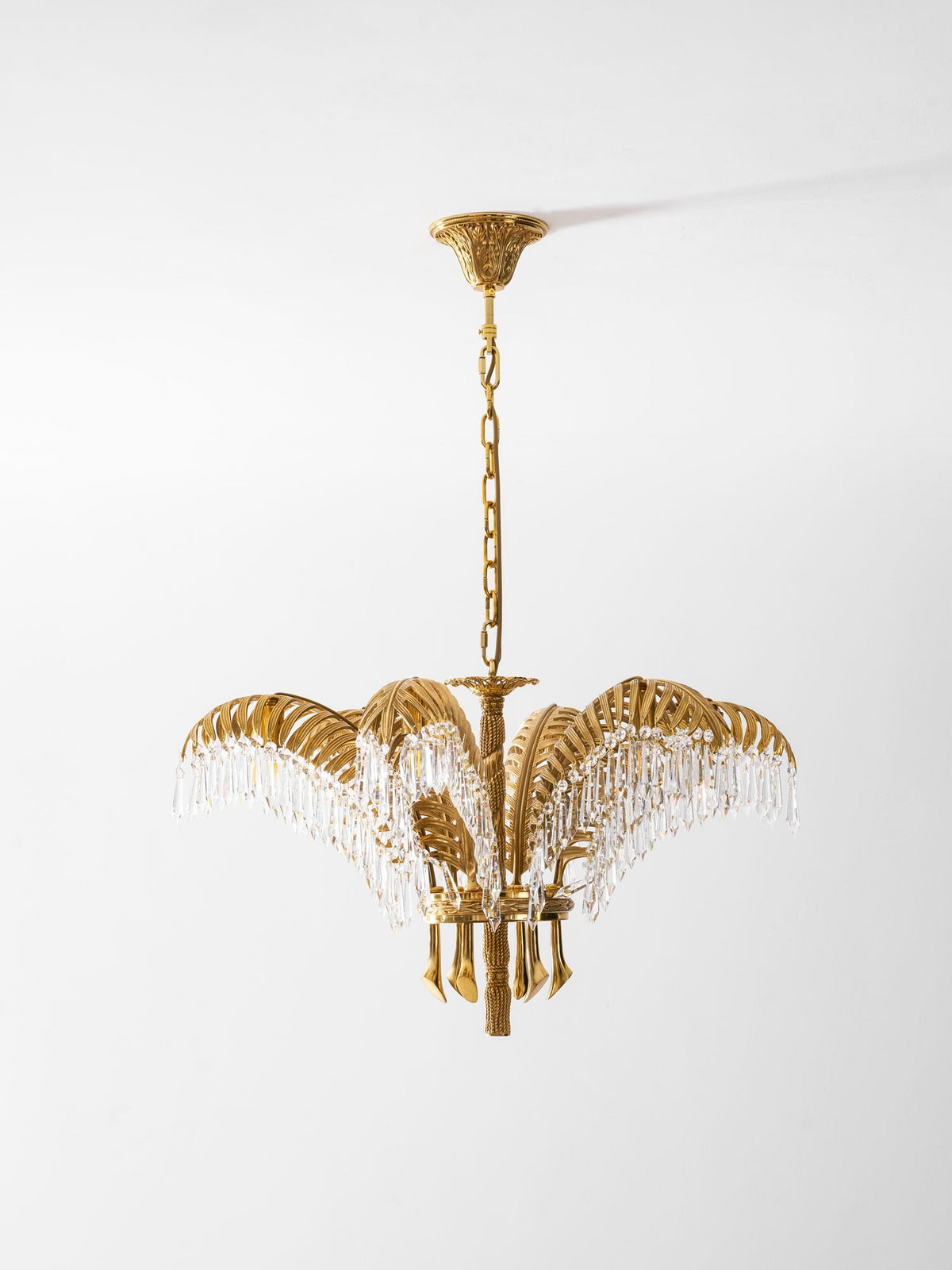 A Clérachic brass chandelier with a carved ceiling plate hangs on a gold chain against a pale grey backdrop.